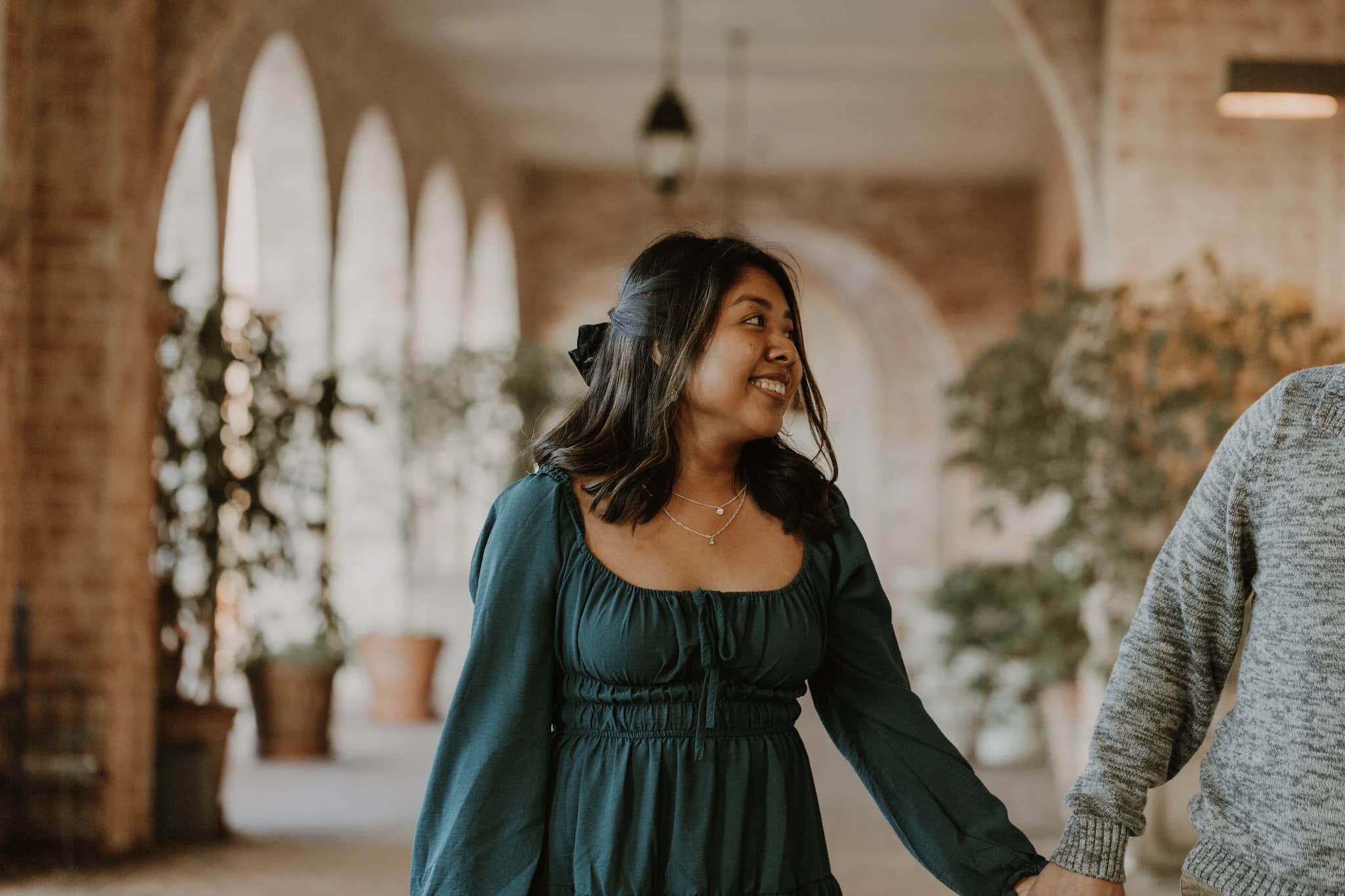 A woman in a green dress looking back beneath a brick arcade