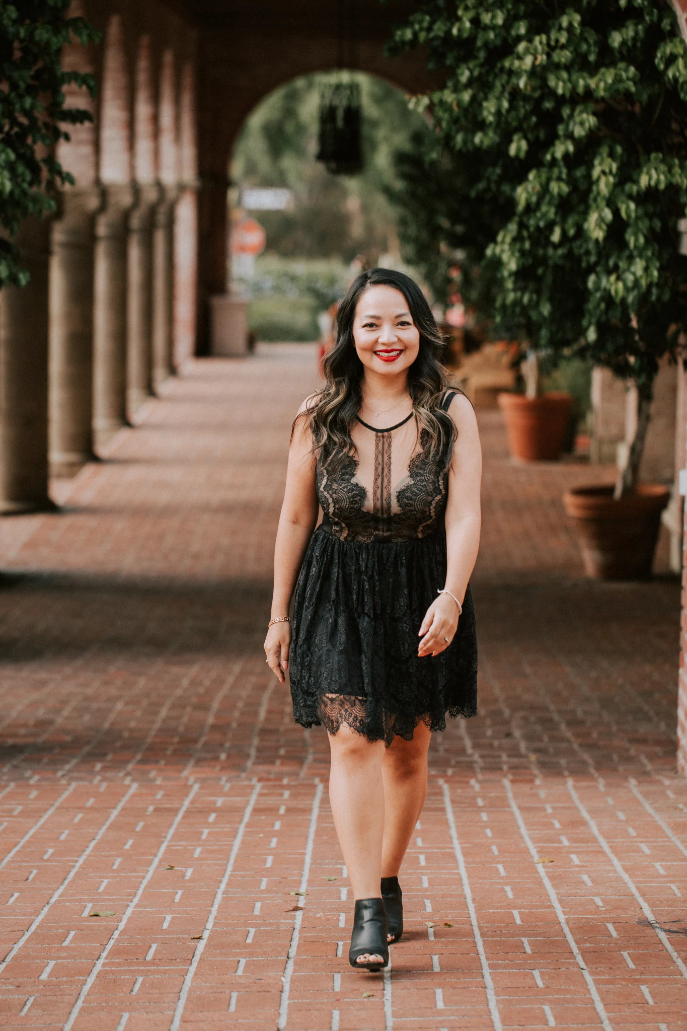 A girl in a black dress smiling in a brick courtyard