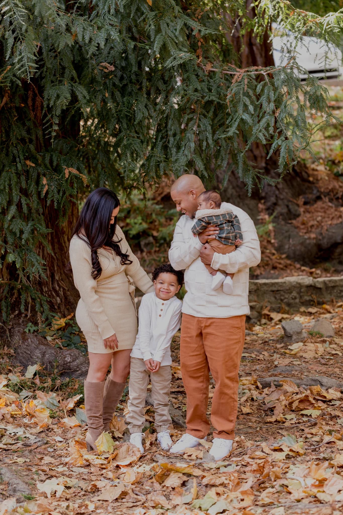 A family standing together on a leaf-covered path beneath the trees